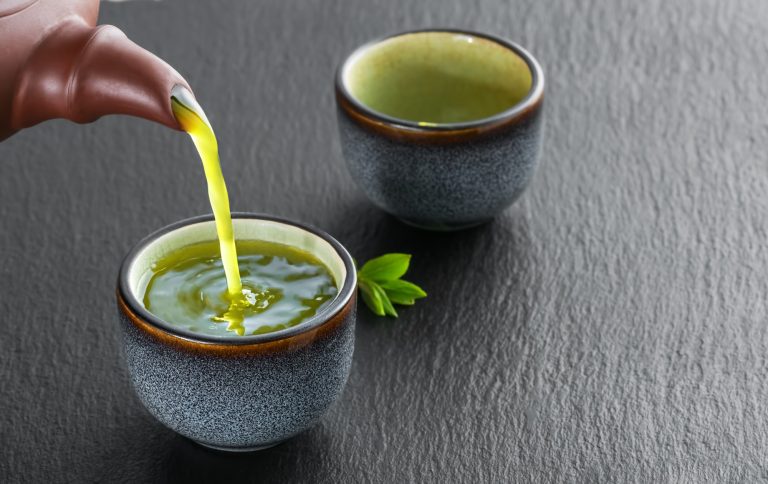 hot green tea is poured from teapot into blue bowl